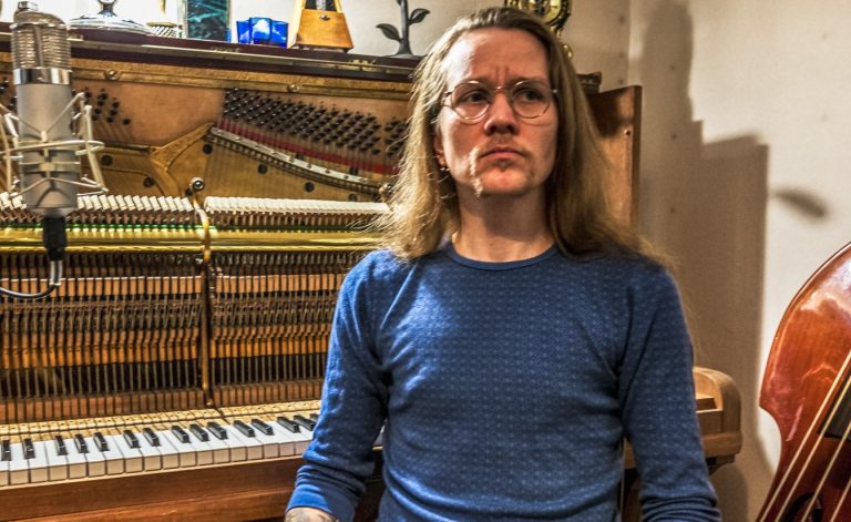 Juha Saunala sitting in front of a piano, next to a cello